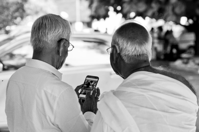 Two men with grey hair and glasses are looking into a phone. It appears that one is showing the other something on the phone.